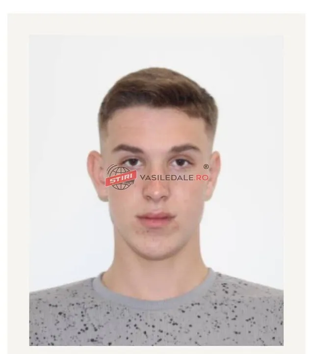 Un bărbat tânăr cu păr scurt și tricou gri cu puncte negre privește spre cameră pe un fundal alb.