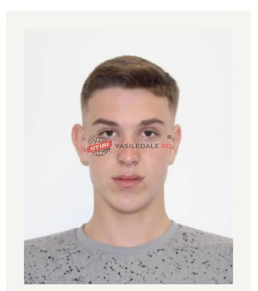 Un bărbat tânăr cu păr scurt și tricou gri cu puncte negre privește spre cameră pe un fundal alb.