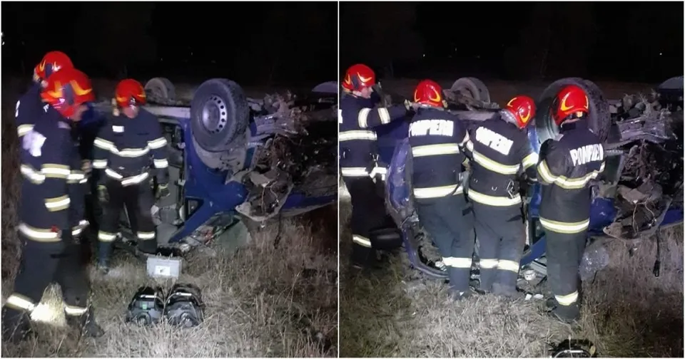 Patru persoane purtând uniforme de pompieri cu benzi reflectorizante stau lângă un vehicul albastru răsturnat pe o zonă cu iarbă, noaptea.