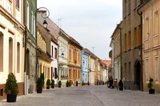 O stradă pietonală este delimitată de clădiri colorate cu ferestre înalte și ghivece cu plante verzi așezate pe trotuar.