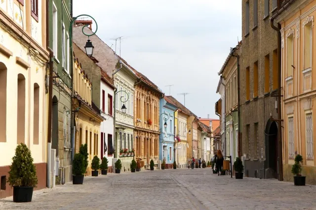O stradă pietonală este delimitată de clădiri colorate cu ferestre înalte și ghivece cu plante verzi așezate pe trotuar.
