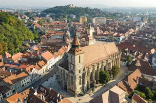 O vedere aeriană a unui oraș cu clădiri cu acoperișuri de țiglă roșie și o biserică mare cu un turn înalt în centru.