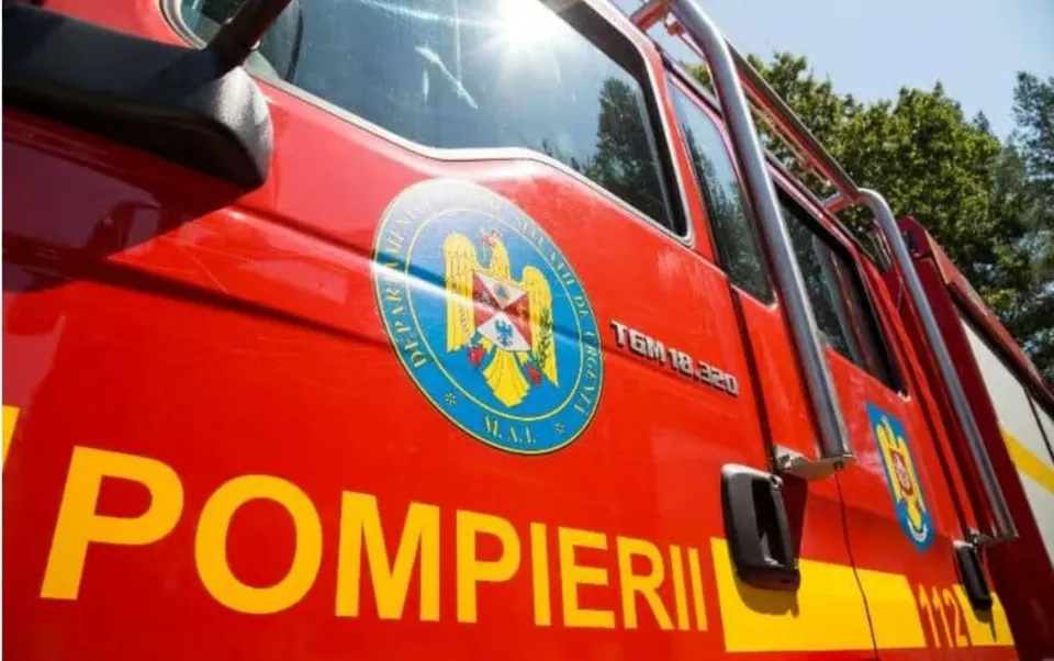 Un vehicul de serviciu roșu prezintă inscripția POMPIERII și un emblema circulară pe lateralul ușii.