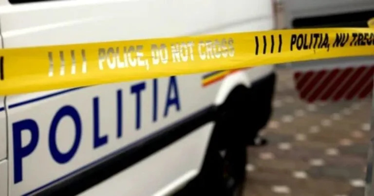 O bandă galbenă de poliție cu inscripții negre este întinsă în fața unui vehicul alb pe care scrie POLITIA cu litere albastre.