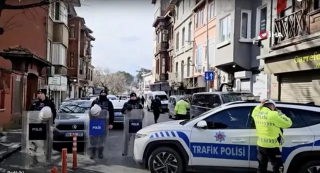 Mai mulți polițiști în uniformă stau lângă mașini de serviciu parcate pe un drum urban cu clădiri pe ambele părți.