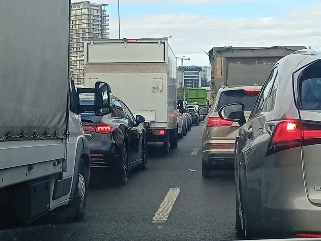 Mai multe mașini și camioane sunt așezate într-un rând pe o porțiune de drum asfaltat sub un cer înnorat.