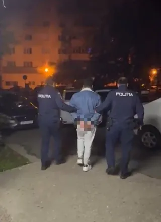 Trei polițiști în uniformă albastră conduc un bărbat îmbrăcat în bluza albastră și pantaloni albi pe un drum asfaltat, noaptea.