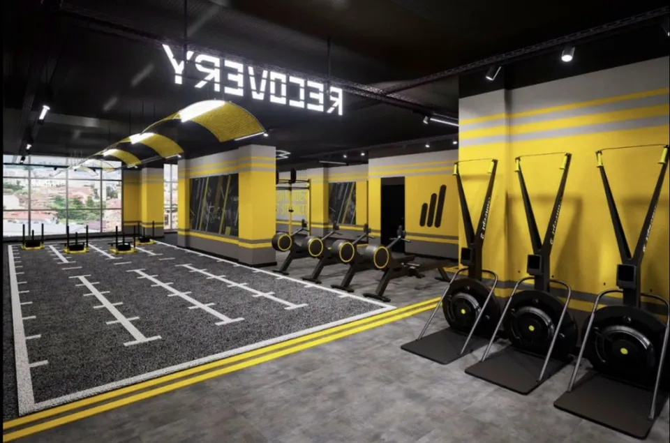 O sală de fitness cu podea neagră marcată cu linii albe, echipamente de antrenament negre și pereți galbeni cu dungi gri.