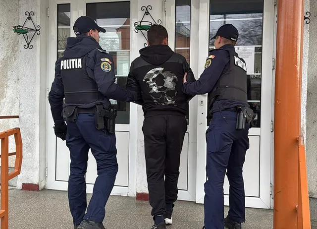Trei polițiști în uniformă întunecată conduc un bărbat cu hanorac negru prin ușa unei clădiri albe.