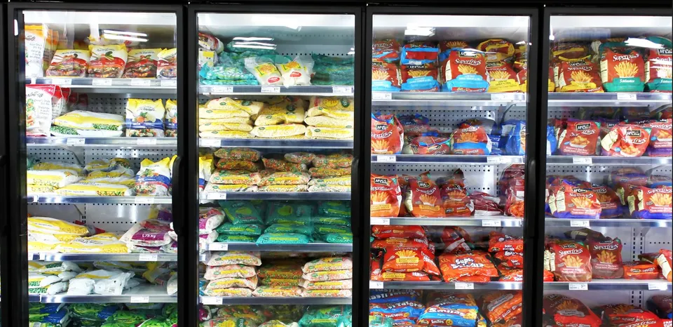 Rânduri de vitrine frigorifice cu uși de sticlă conținând diverse produse alimentare ambalate în pungi și cutii colorate.