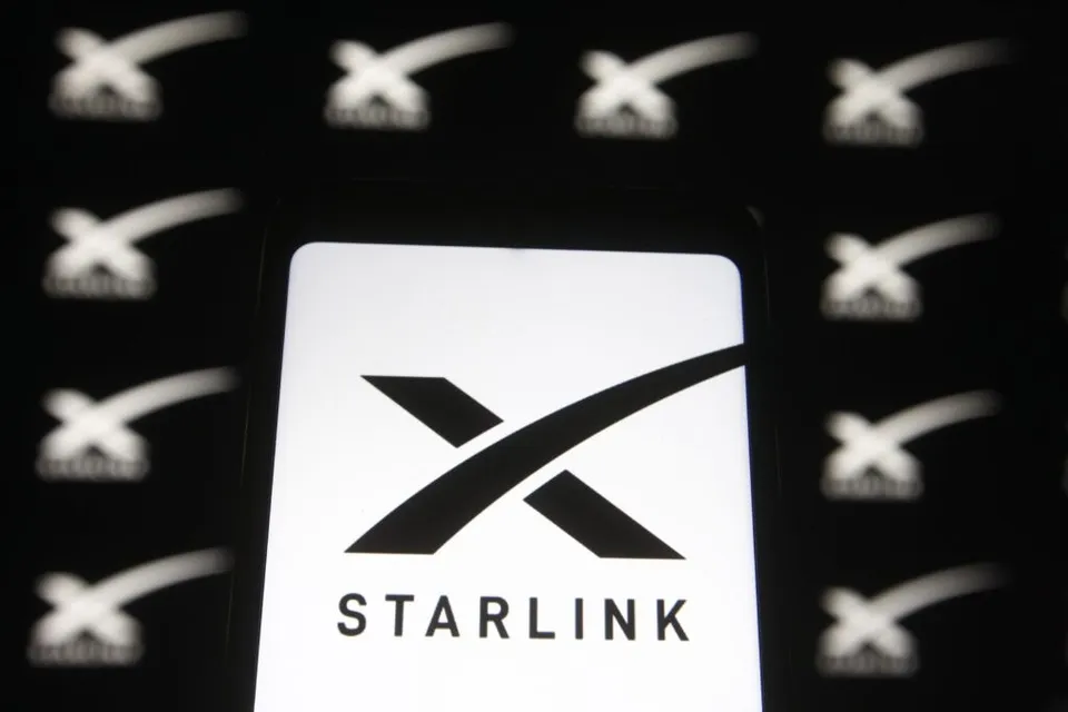 Un ecran de dispozitiv luminos afișează logo-ul alb al Starlink pe un fundal negru, înconjurat de mai multe simboluri similare repetate în fundal.