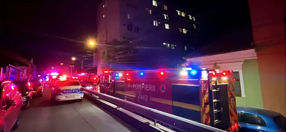 Vehicule de intervenție cu luminile roșii și albastre aprinse, o scară lungă extinsă și o stradă luminată pe nocturn.