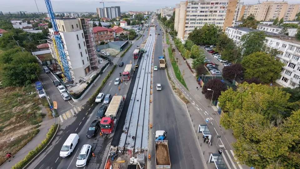 O vedere de sus prezintă o stradă cu șantier, utilaje de construcții, mașini și clădiri de apartamente pe ambele părți ale drumului.