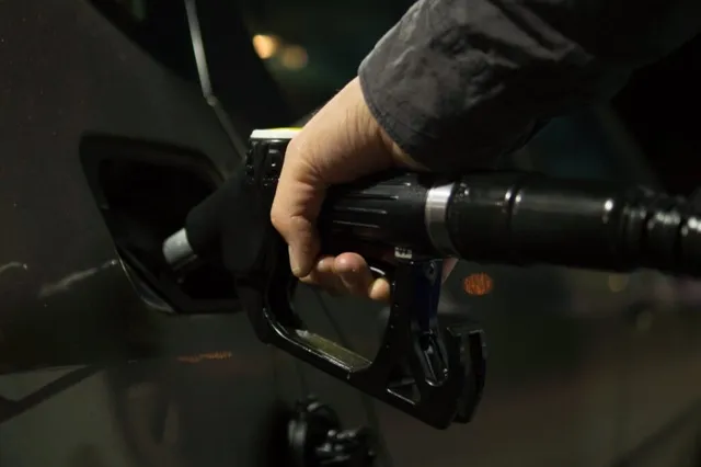O mână ține un pistol de pompat combustibil introdus în orificiul de umplere al unui vehicul în timpul nopții.