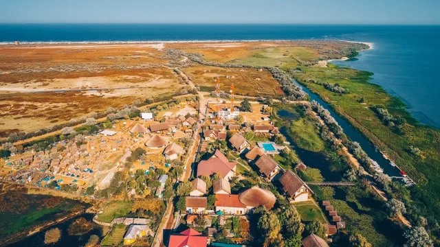 O vedere aeriană prezintă un grup de clădiri cu acoperișuri colorate, vegetație și un canal de apă lângă o zonă de coastă vastă.