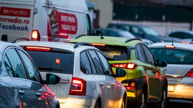 Mai multe mașini sunt așezate în trafic pe un drum, fiind vizibile farurile și luminile de frână ale vehiculelor.