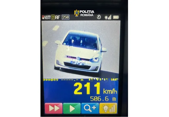 O mașină albă este surprinsă pe un ecran de dispozitiv de măsurare a vitezei, afișând cifra 211 km/h pe un fundal albastru.