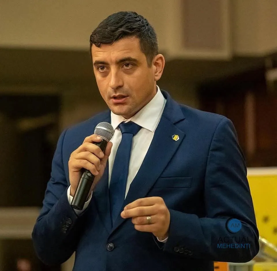 Un bărbat cu părul scurt și costum albastru, cămașă albă și cravată albastră, ține un microfon argintiu în mână.