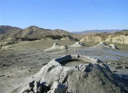 Un con de noroi gri cu o cavitate plină de apă se află într-un peisaj arid cu dealuri sub un cer senin.