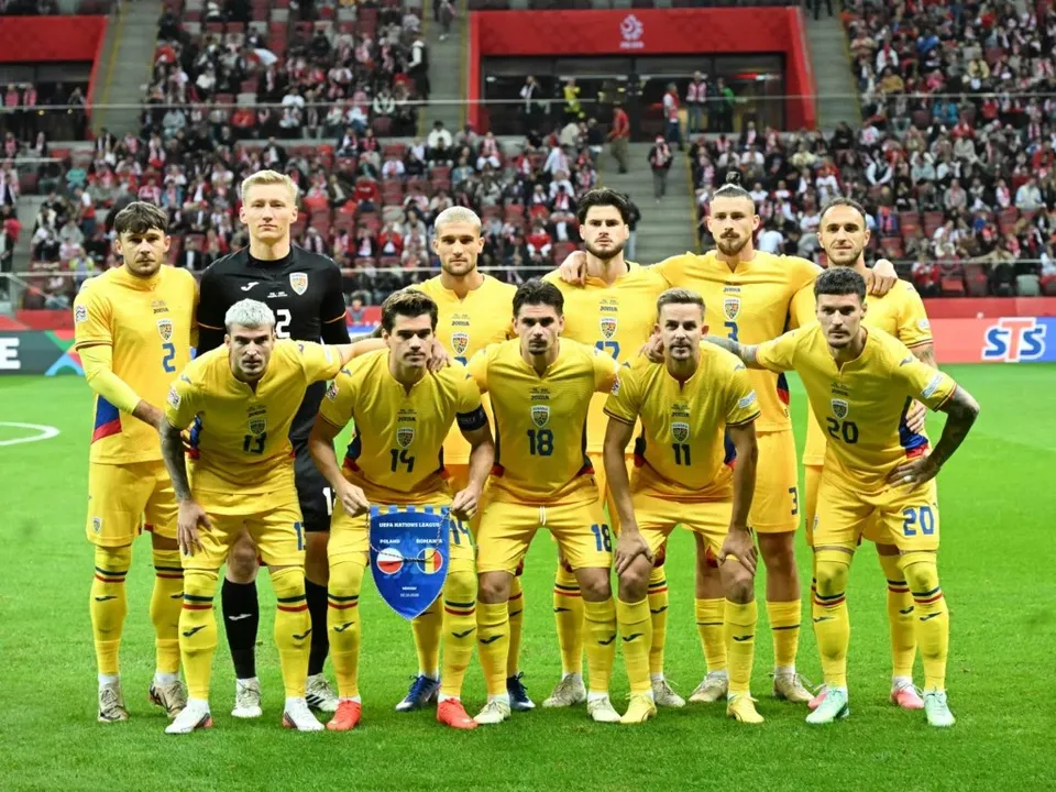 O echipă de fotbaliști în echipament galben stă în poziție de pregătire pe un teren de fotbal în fața unui stadion plin de spectatori.