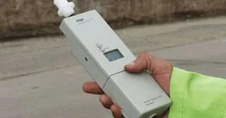 O mână ține un aparat electronic de culoare gri cu un ecran digital și un embucătură albă.