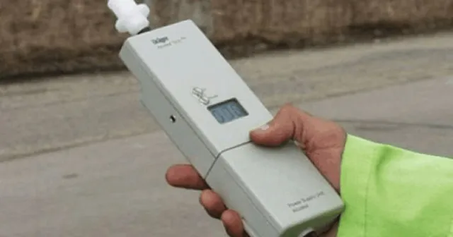 O mână ține un aparat electronic de culoare gri cu un ecran digital și un embucătură albă.