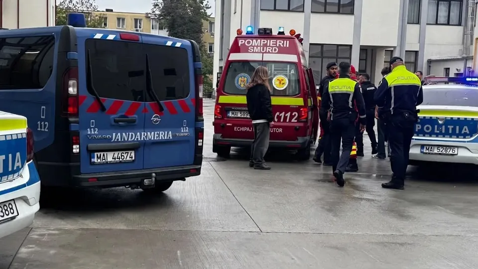 Vehiculele jandarmeriei, ale poliției și ale serviciului SMURD sunt parcate pe o suprafață pavată lângă o clădire, înconjurate de mai mulți agenți în uniformă.