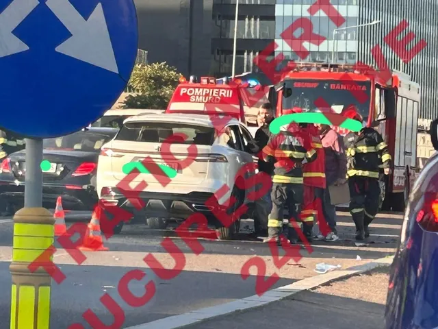 Echipaje de pompieri și salvatori stau lângă un vehicul alb și un camion de pompieri pe o stradă cu trafic.