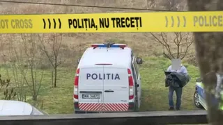 O mașină de poliție albă este parcată pe un drum, lângă un cordon de poliție galben și o persoană cu fața acoperită.