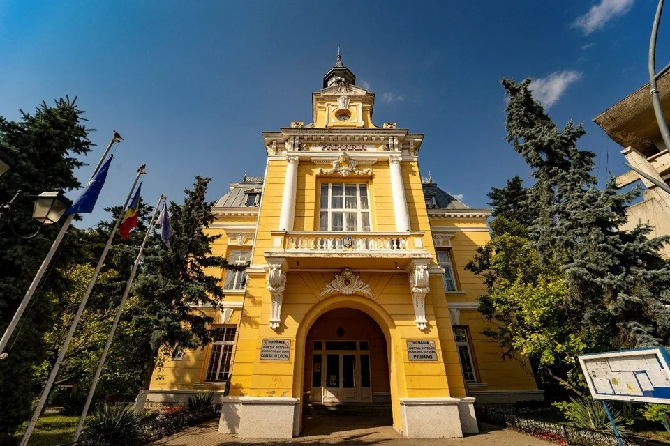 O clădire galbenă cu arhitectură clasică, având ferestre mari, un balcon alb și steaguri montate pe stâlpi în partea stângă.