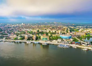 O vedere aeriană a unui oraș cu clădiri diverse, vegetație și un râu cu câteva embarcațiuni la mal.