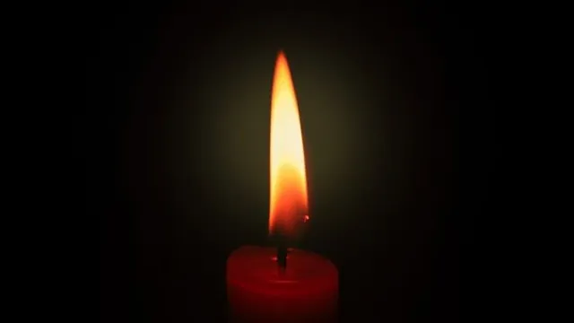 O lumânare roșie aprinsă arde într-un fundal negru întunecat.