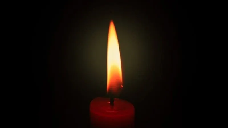 O lumânare roșie aprinsă arde într-un fundal negru întunecat.