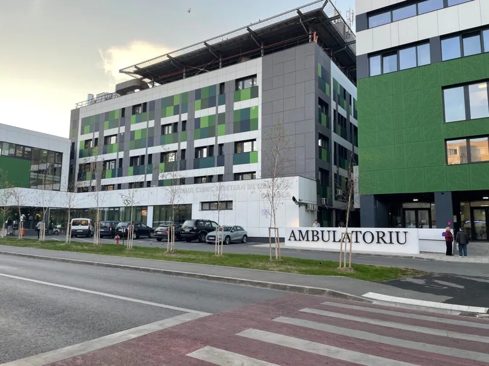 O clădire modernă cu fațadă gri și verde prezintă un conținut marcat cu textul AMBULATORIU lângă un drum cu trecere de pietoni.