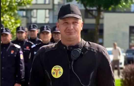 Un bărbat în uniformă neagră cu un emblema galbenă pe piept stă în prim-plan, în fața unui grup de bărbați în uniformă similară.