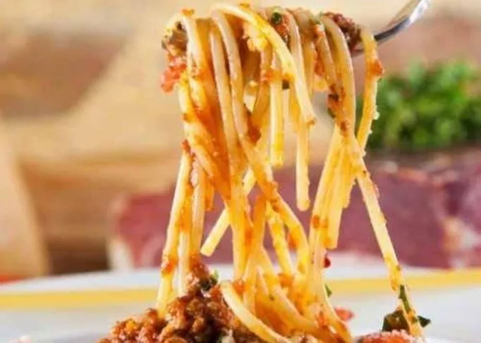 Forte de spaghete cu sos de roșii și bucăți de carne sunt ridicate cu o furculiță pe un fundal neclar.