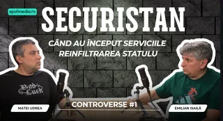 Doi bărbați stau la o masă cu microfoane în fața unui perete de cărămidă gri, purtând tricouri negru și verde.