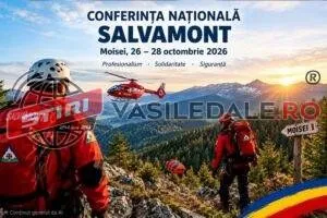 Un salvamontaj cu echipament de protecție portînd un rucsac observă un elicopter roșu deasupra unui peisaj montan împădurit sub un cer luminos.