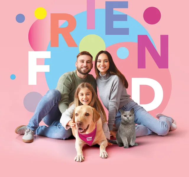 O familie formată din un bărbat, o femeie și o fetiță stă așezată pe un fundal roz alături de un câine și o pisică.
