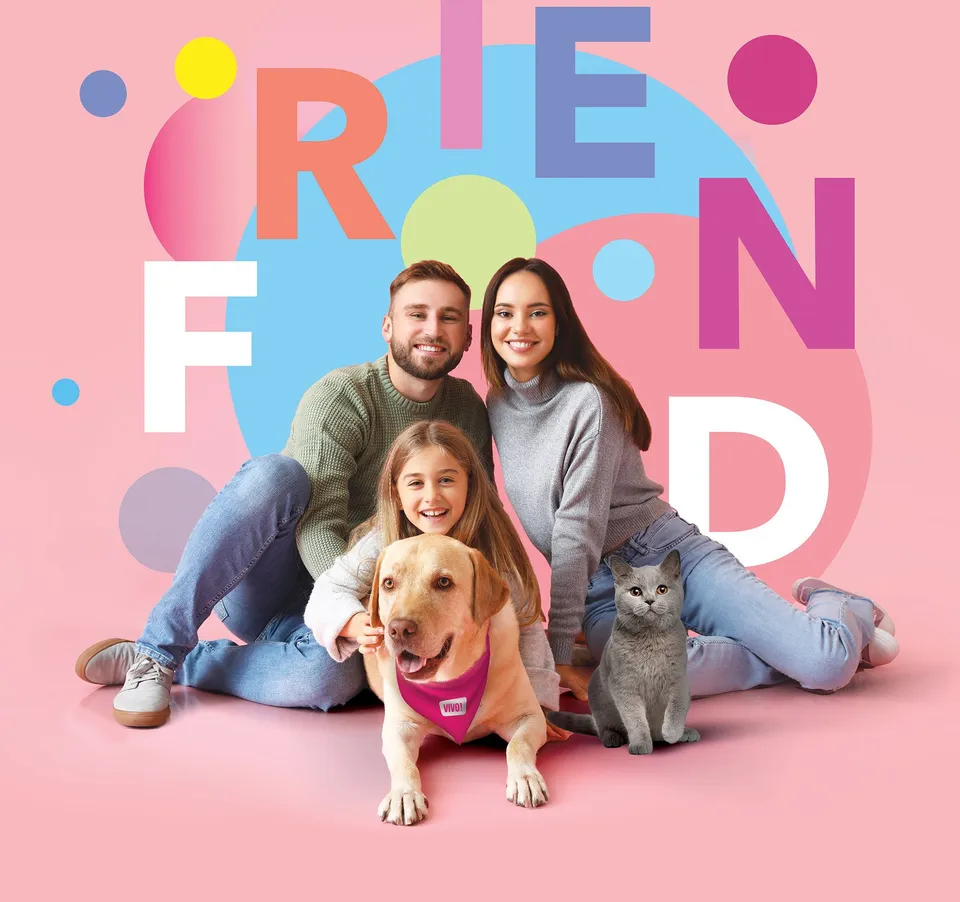 O familie formată din un bărbat, o femeie și o fetiță stă așezată pe un fundal roz alături de un câine și o pisică.