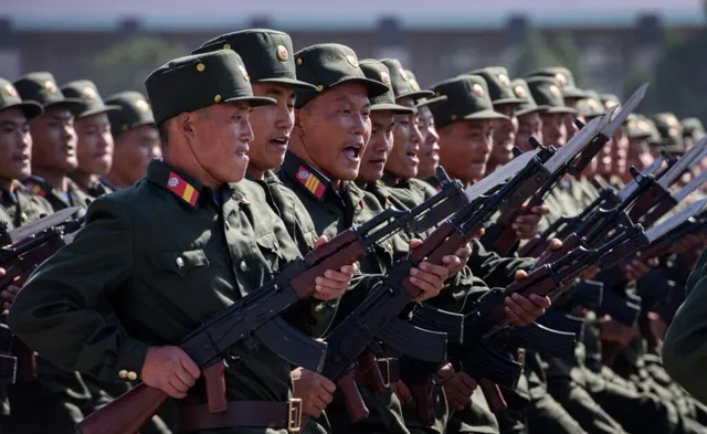 O linie de soldați în uniformă verde și pălării militare poartă puști cu baionete în timpul unei formațiuni.
