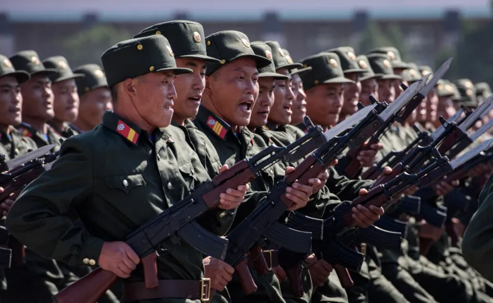 O linie de soldați în uniformă verde și pălării militare poartă puști cu baionete în timpul unei formațiuni.
