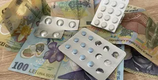 Mai multe blistere cu tablete albe sunt așezate peste diverse bancnote românești pe o suprafață de lemn.