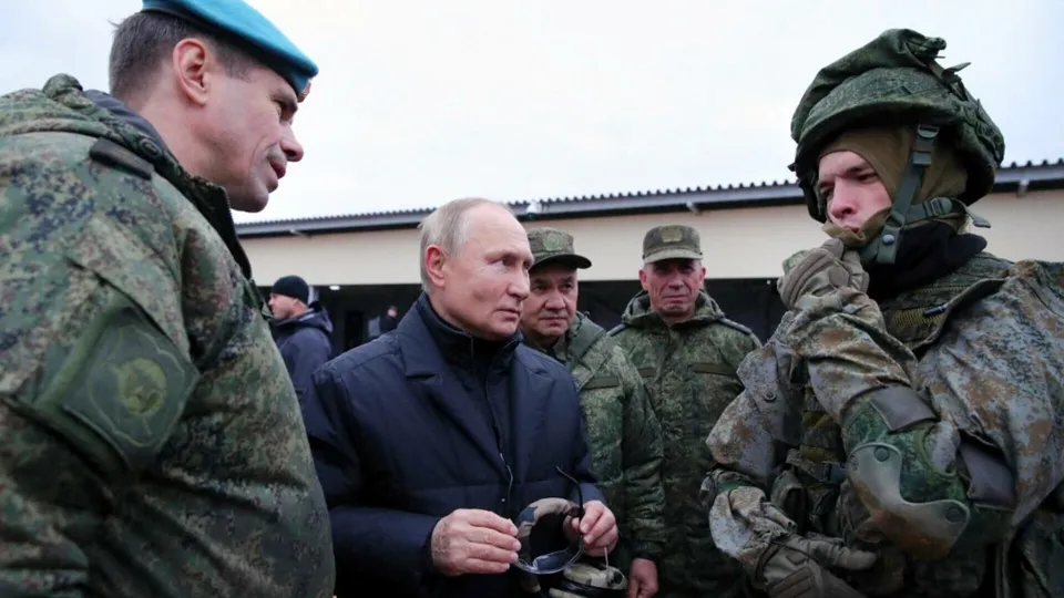 Un bărbat în haine civile este înconjurat de bărbați în uniforme militare și capacuri într-un spațiu exterior.