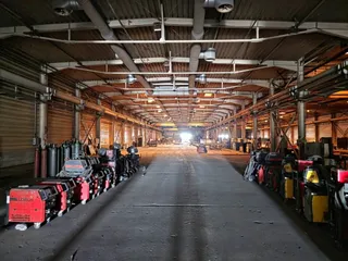 Interiorul unei hale industriale cu un coridor central liber și diverse utilaje de curățenie aliniate pe ambele părți ale drumului.