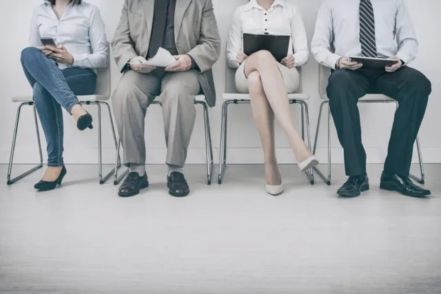 Patru persoane stau așezate pe scaune aliniate, folosind telefoane mobile sau tablete, purtând haine de business.