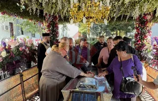 Oameni stau în jurul unui obiect de sticlă sub un copertin decorat cu flori și un candelabru de aur.