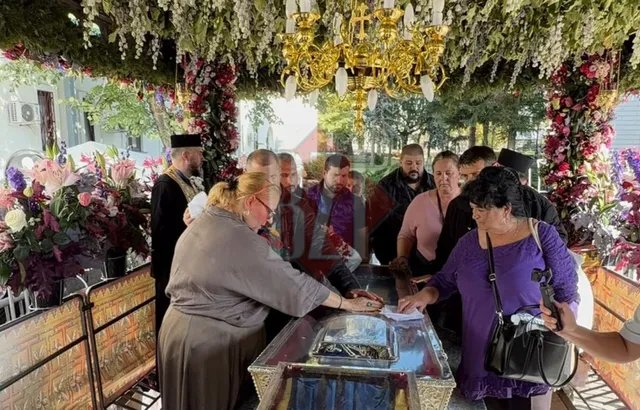 Oameni stau în jurul unui obiect de sticlă sub un copertin decorat cu flori și un candelabru de aur.