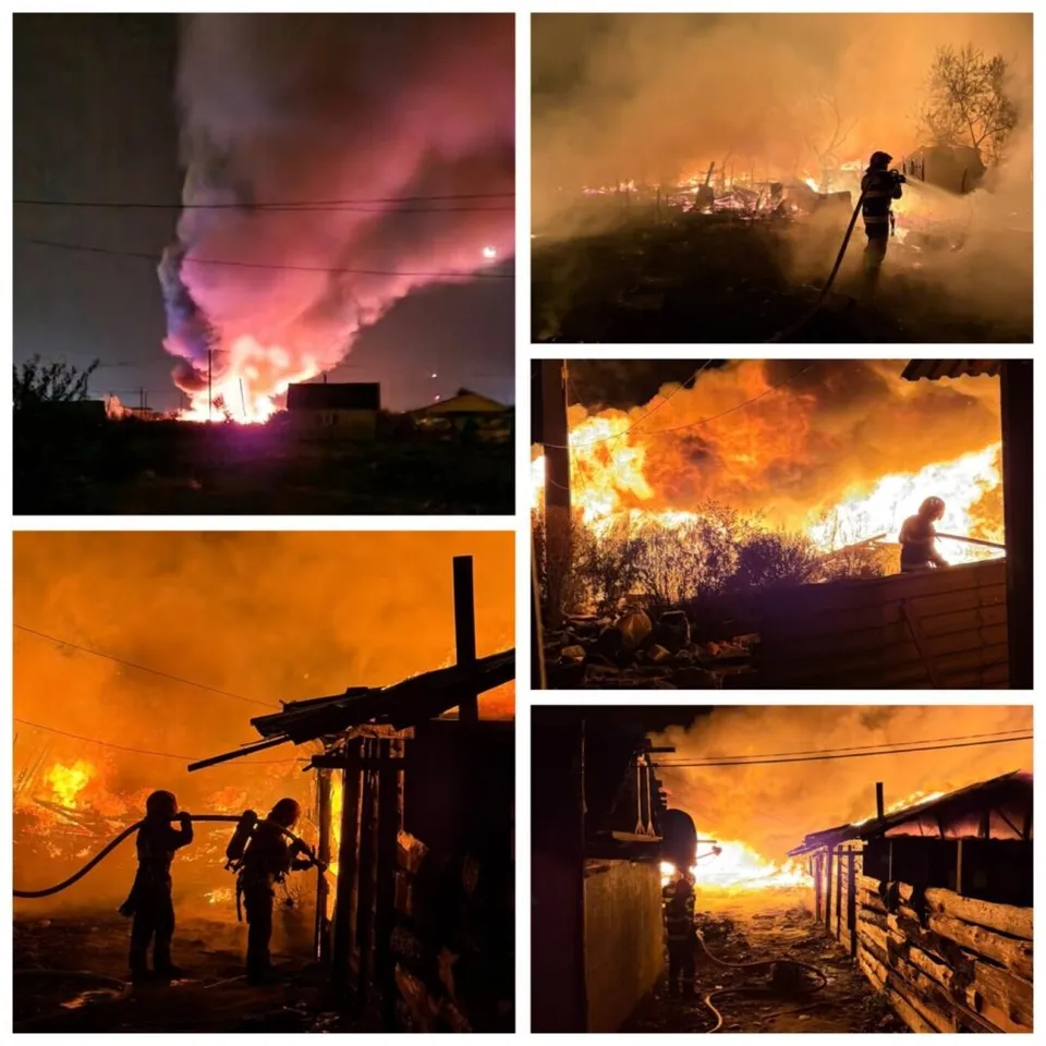 Siluete de pompieri luptă cu flăcările și fumul dens în fața unor structuri de lemn în timpul nopții.