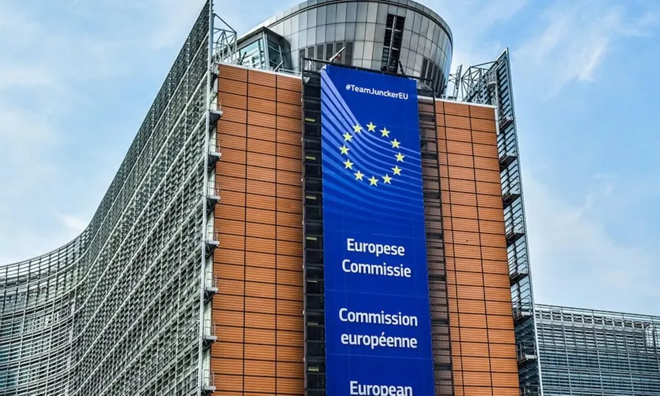 O clădire modernă cu fațadă de sticlă și panouri maro este parțial acoperită de un banner albastru pe care apare steagul european și text scris.